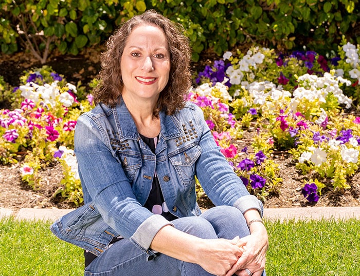 A beautiful headshot of a woman with flowers in the background.