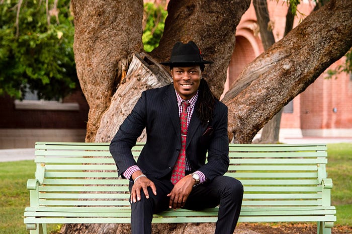 A portrait of an African American man sitting on a park bench smiling.
