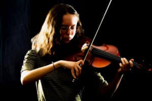 A portrait photo of a kid playing a viola in the dark.